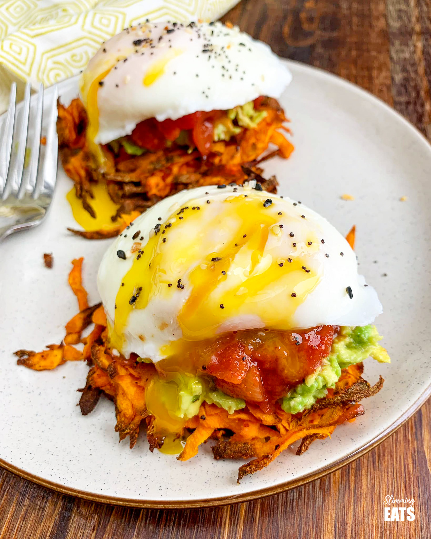 poached eggs over salsa, mashed avocado and sweet potato hash browns on brown rimmed cream plate