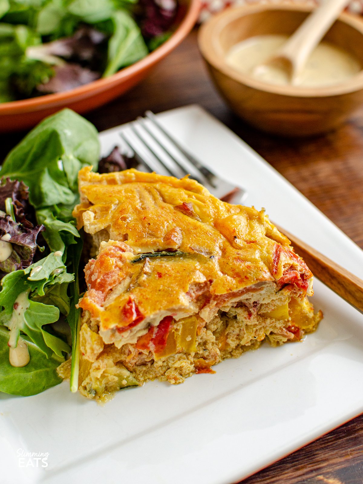 Enjoy a delicious and healthy alternative to the classic quiche. This dairy free crustless bacon vegetable quiche is packed with protein and flavourful vegetables and is perfect for those who need to avoid dairy. slice of Dairy Free Crustless Bacon and Vegetable Quiche on white plate with salad