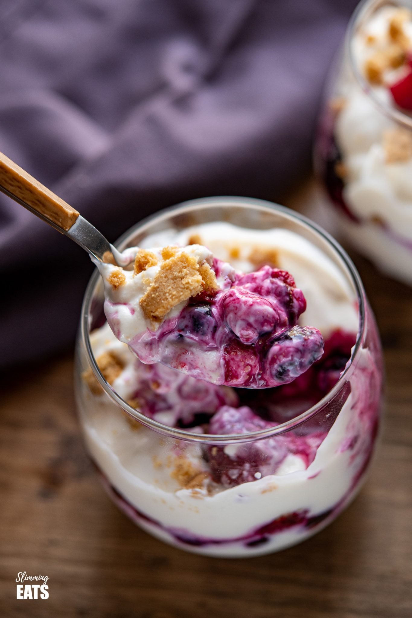 Fruity Yoghurt Shortbread Sundae - a Delicious combination of mixed berries, lemon flavoured Greek yoghurt and crumbled shortbread for a perfect after dinner dessert. Slimming Eats and Weight Watchers friendly wooden handled spoon spooning out some Fruity Yoghurt Shortbread Sundae from a stemless wine glass