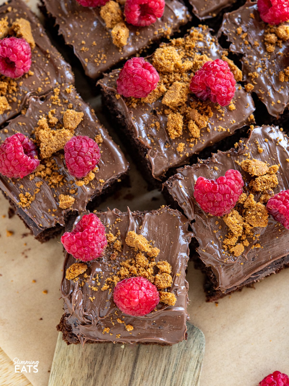 Love a slice of guilt-free cake? Check out this delicious low calorie chocolate cake for only 158 calories a slice, topped with nutella spread, crumbled lotus biscoff cookies and fresh raspberries. close up of sliced Raspberry Nutella Chocolate Cake on a wooden board with scattered raspberries