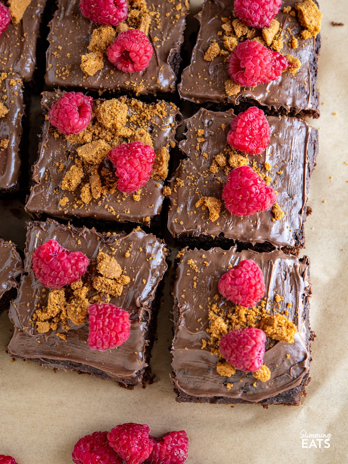 Love a slice of guilt-free cake? Check out this delicious low calorie chocolate cake for only 158 calories a slice, topped with nutella spread, crumbled lotus biscoff cookies and fresh raspberries. close up of sliced Raspberry Nutella Chocolate Cake on a wooden board with scattered raspberries