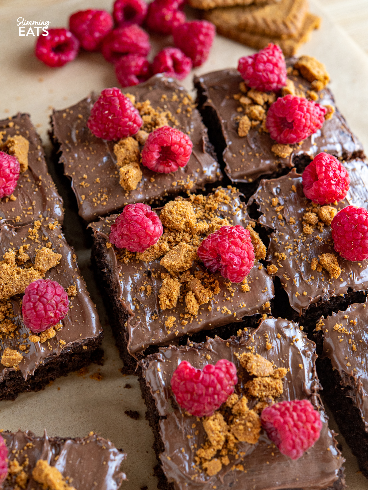 close up of sliced Raspberry Nutella Chocolate Cake on a wooden board with scattered raspberries and lotus cookies