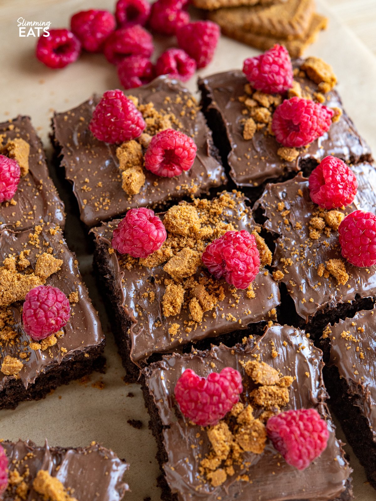 Love a slice of guilt-free cake? Check out this delicious low calorie chocolate cake for only 158 calories a slice, topped with nutella spread, crumbled lotus biscoff cookies and fresh raspberries. close up of sliced Raspberry Nutella Chocolate Cake on a wooden board with scattered raspberries and lotus cookies