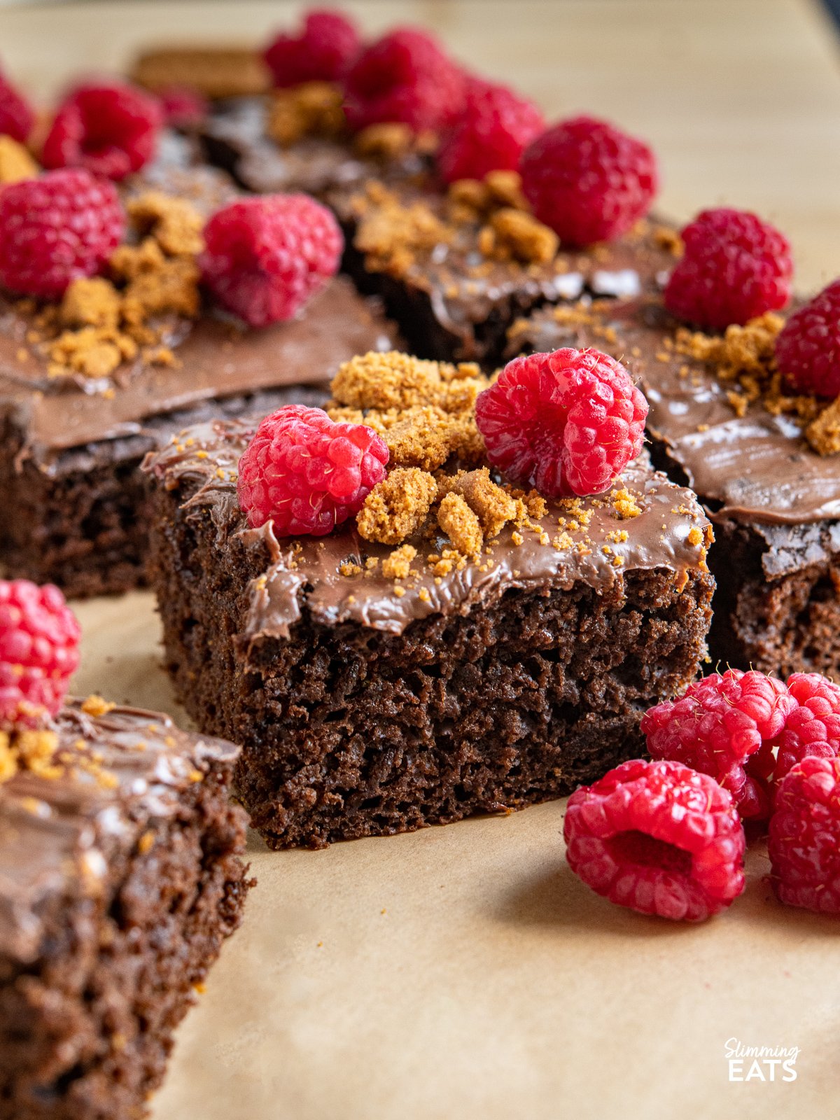 Love a slice of guilt-free cake? Check out this delicious low calorie chocolate cake for only 158 calories a slice, topped with nutella spread, crumbled lotus biscoff cookies and fresh raspberries. close up of slice of Raspberry Nutella Chocolate Cake with raspberries in front and other slices behind