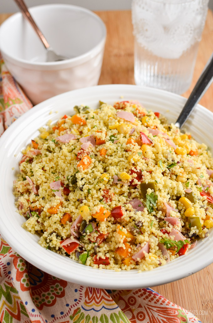 roasted vegetables and ham couscous in a white bowl with glass of water