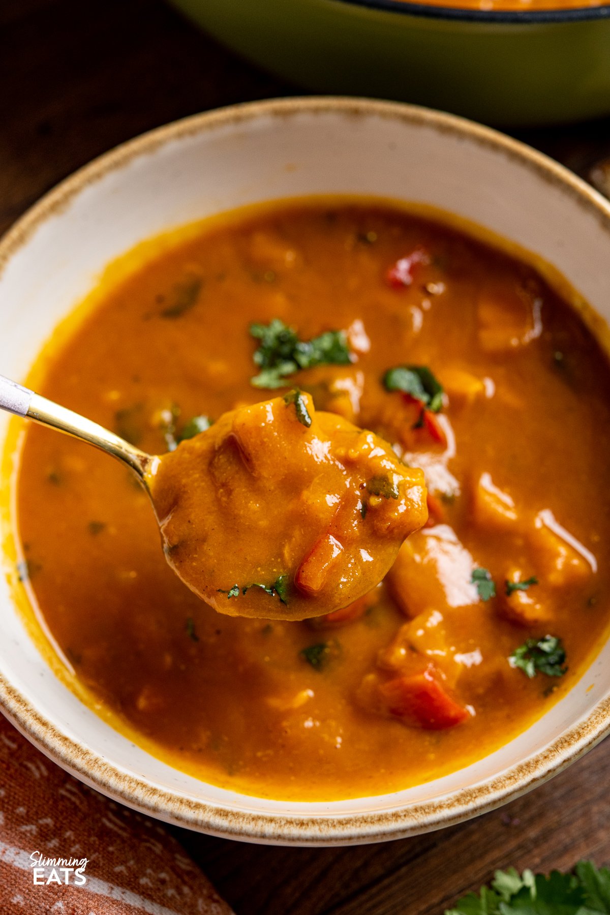 Spicy Sweet Potato, Red Pepper and Carrot Soup - a hearty low calorie soup with the natural sweetness from sweet potato paired with the spicy kick from a blend of spices making it both flavourful and delicious. close up of a spoon of Sweet Potato, Red Pepper and Carrot Soup on a spoon from bowl.