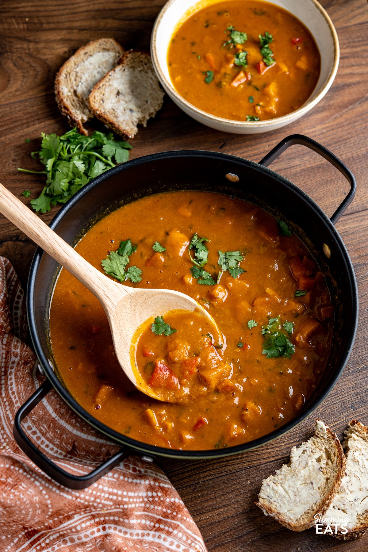 Sweet Potato, Red Pepper and Carrot Soup in a black double handled pan with wooden spoon