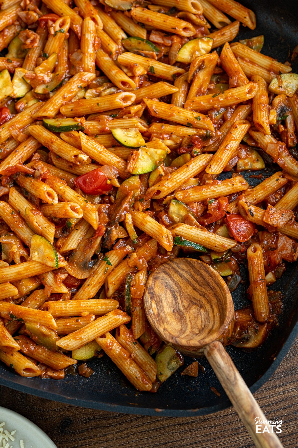 Delicious speedy Mushroom, Bacon, Tomato and Zucchini Pasta - a simple but delicious pasta recipe that the whole family will love. Gluten Free, dairy free, Slimming Eats and Weight Watchers friendly close up of Mushroom, Bacon, Tomato and Zucchini Pasta in square all-clad skillet with olive wood spoon