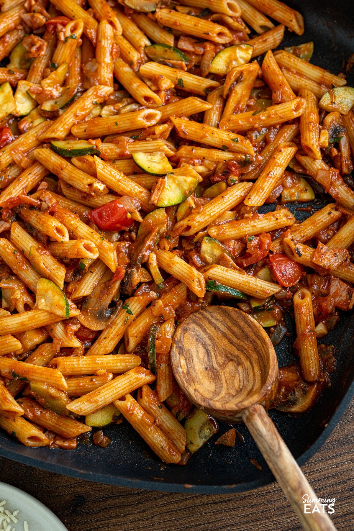 close up of Mushroom, Bacon, Tomato and Zucchini Pasta in square all-clad skillet with olive wood spoon