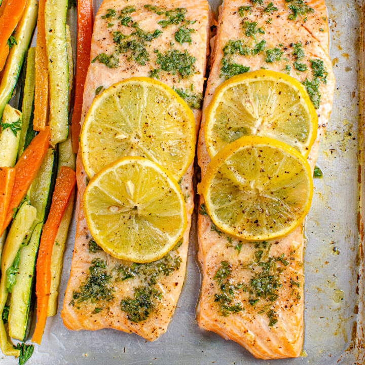 Lemon and Herb Butter Salmon topped with lemon slices with carrot and zucchini batons on a white plate on baking tray