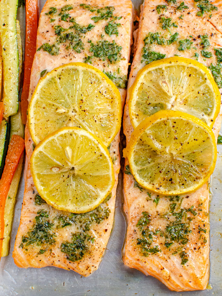 Lemon and Herb Butter Salmon topped with lemon slices with carrot and zucchini batons on a white plate on baking tray