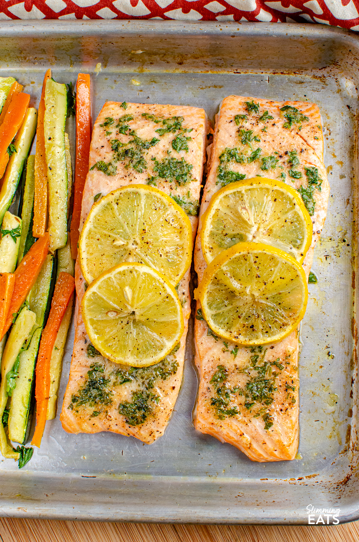 Lemon and Herb Butter Salmon topped with lemon slices with carrot and zucchini batons on a baking sheet