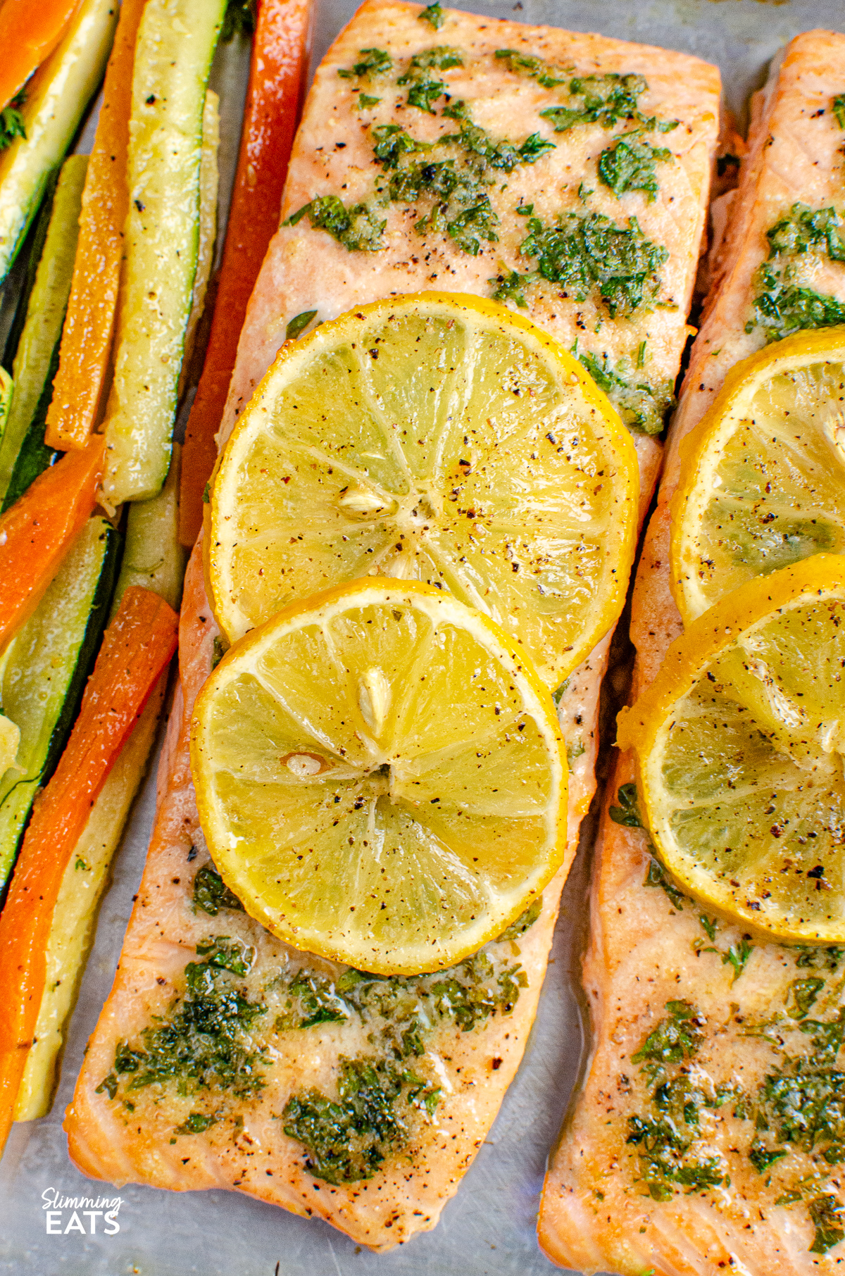 close up of Lemon and Herb Butter Salmon topped with lemon slices with carrot and zucchini batons on a baking sheet