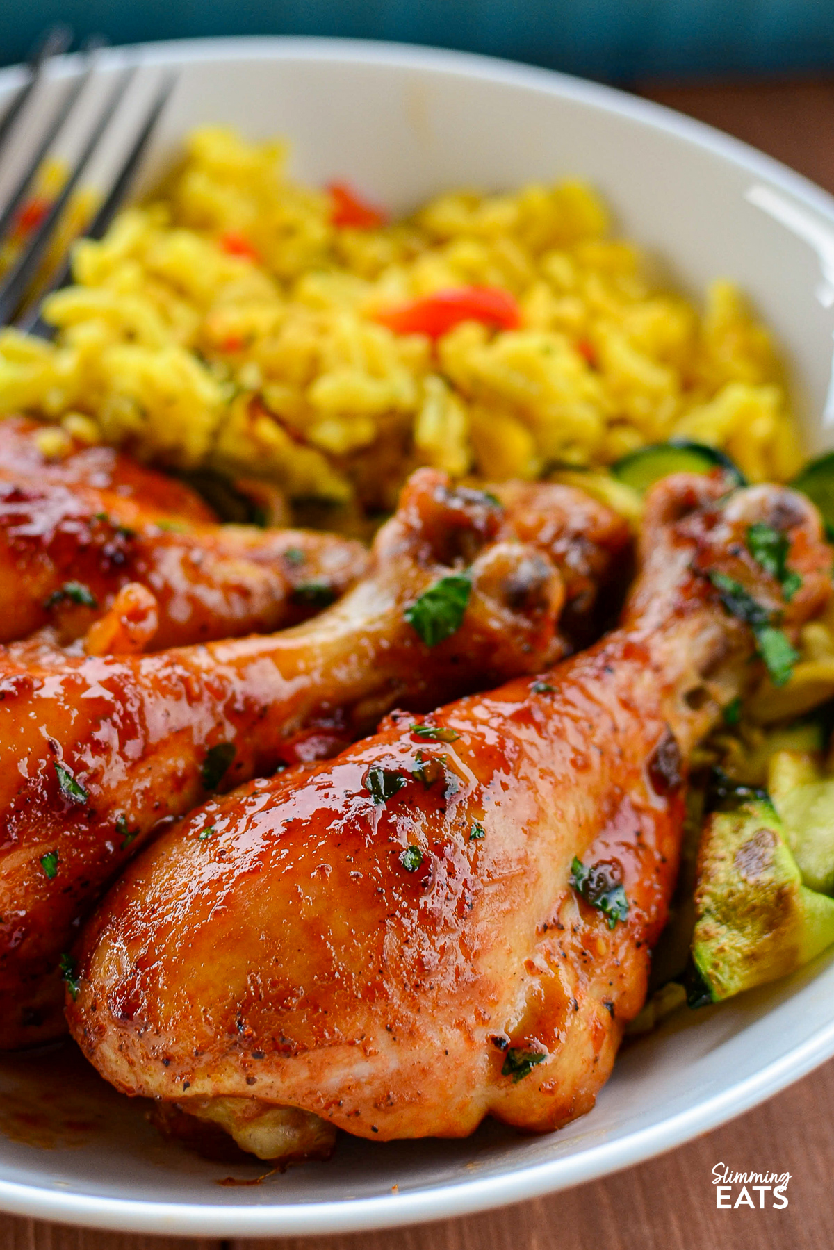 close up of Cooked Maple Glazed Chicken drumsticks in a white bowl with veggie sand rice
