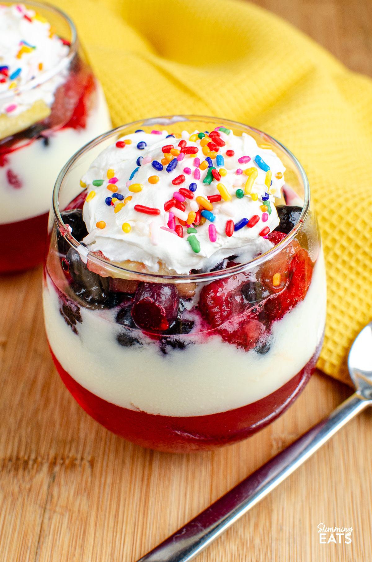 Skinny Trifle in a stemless wine glass with layers of jelly, yoghurt, fruit and light aerosol cream topped with sprinkles