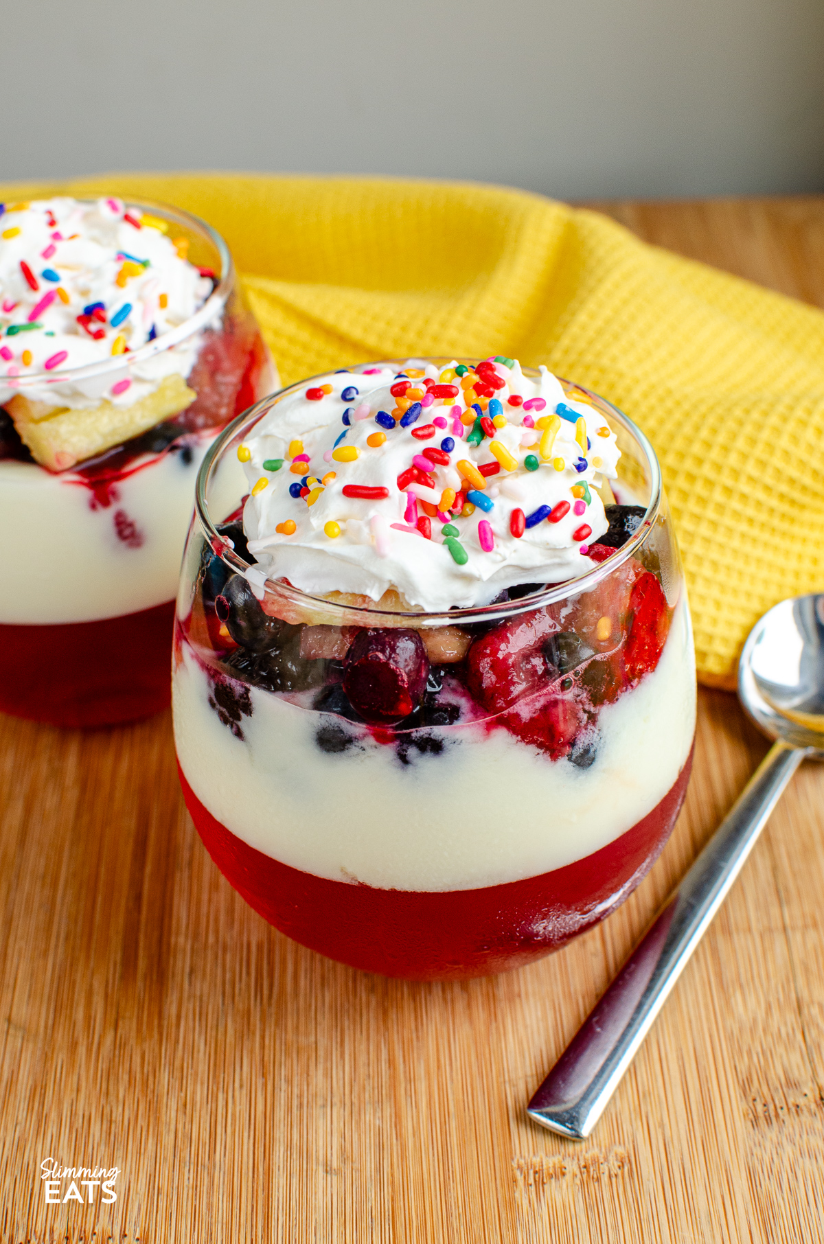 Skinny Trifle in a stemless wine glass with layers of jelly, yoghurt, fruit and light aerosol cream topped with sprinkles