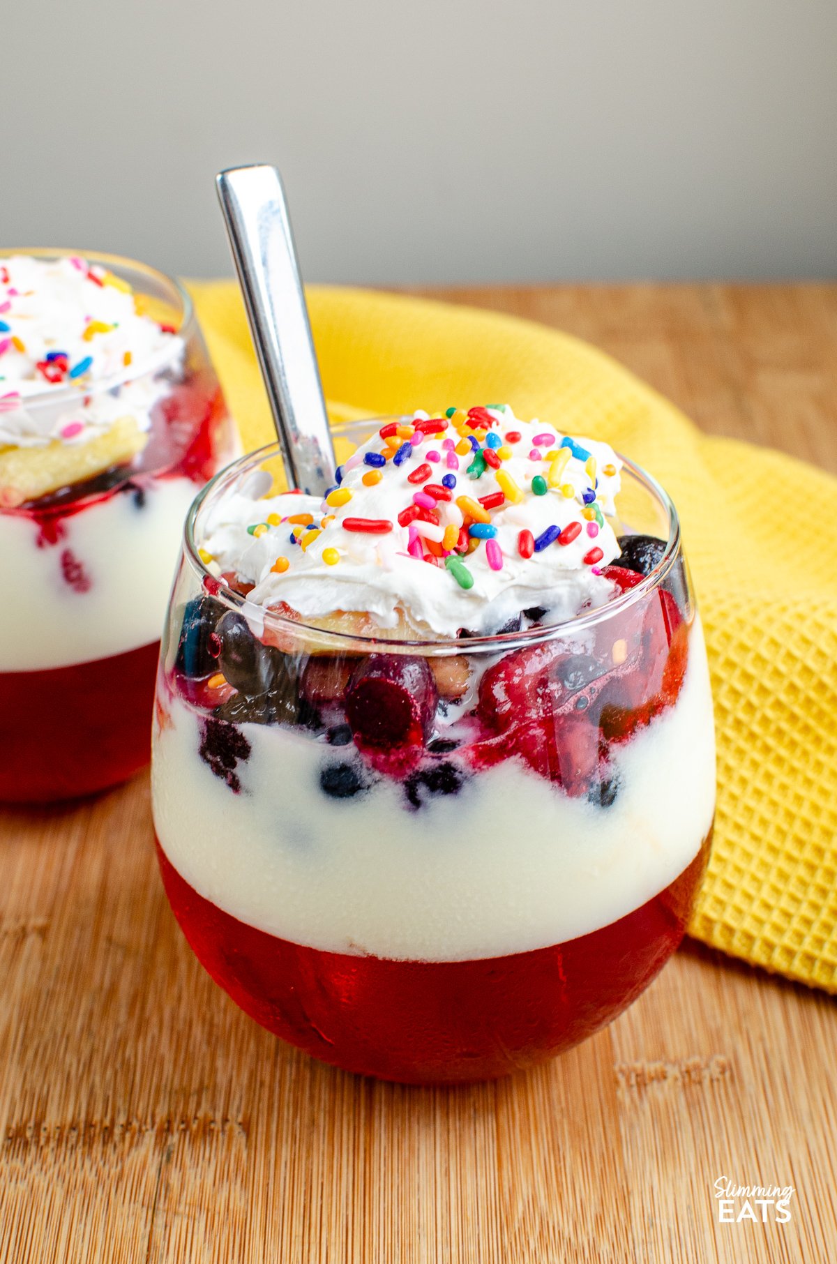 Skinny Trifle in a stemless wine glass with layers of jelly, yoghurt, fruit and light aerosol cream topped with sprinkles