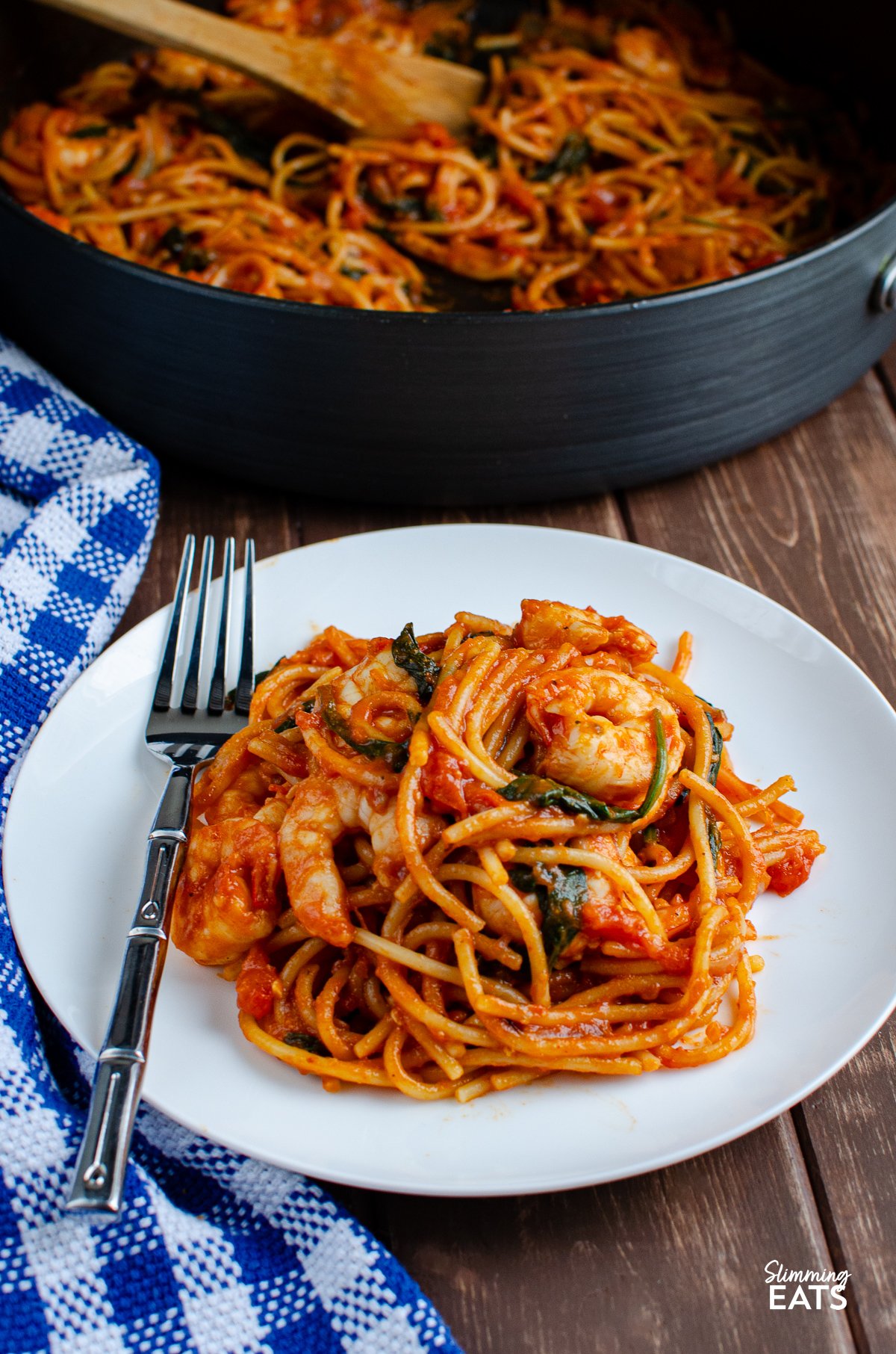 Shrimp and Spinach Tomato Pasta served on a pristine white plate, with a fork poised on the side. In the background, a pan hints at the dish's one-pot simplicity.