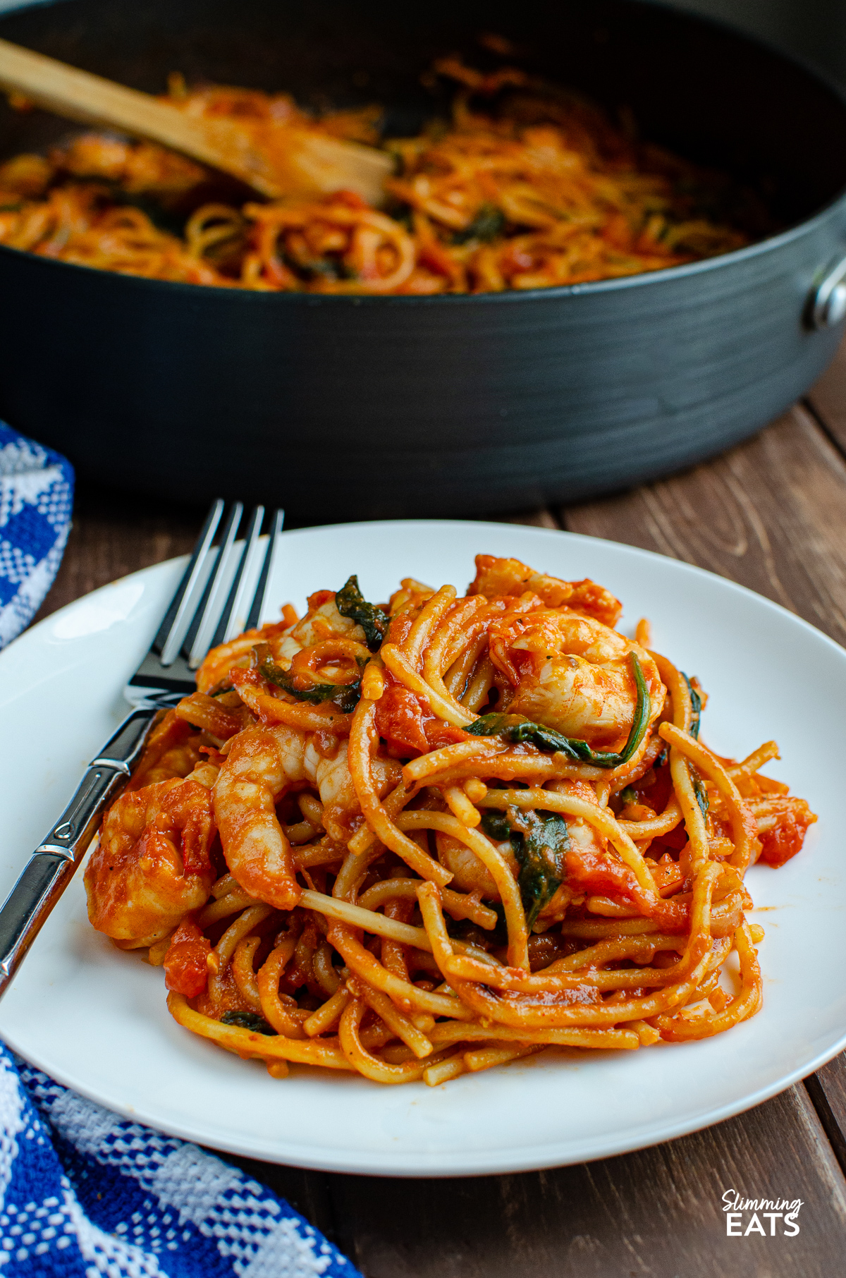 Shrimp and Spinach Tomato Pasta served on a pristine white plate, with a fork poised on the side. In the background, a pan hints at the dish's one-pot simplicity.