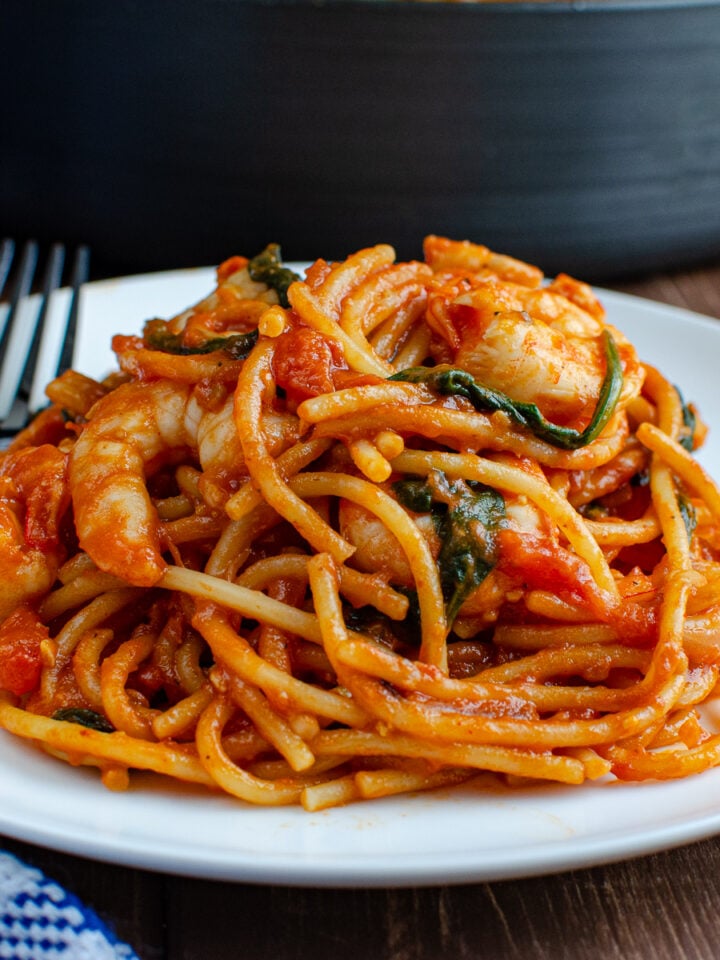 Shrimp and Spinach Tomato Pasta served on a pristine white plate, with a fork poised on the side. In the background, a pan hints at the dish's one-pot simplicity.