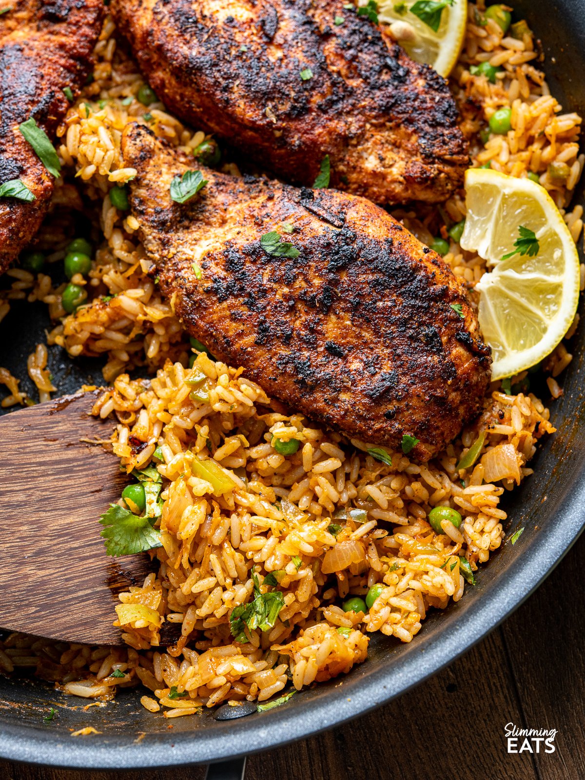 close up of Spanish Chicken and Rice in a black frying pan with wooden spatula