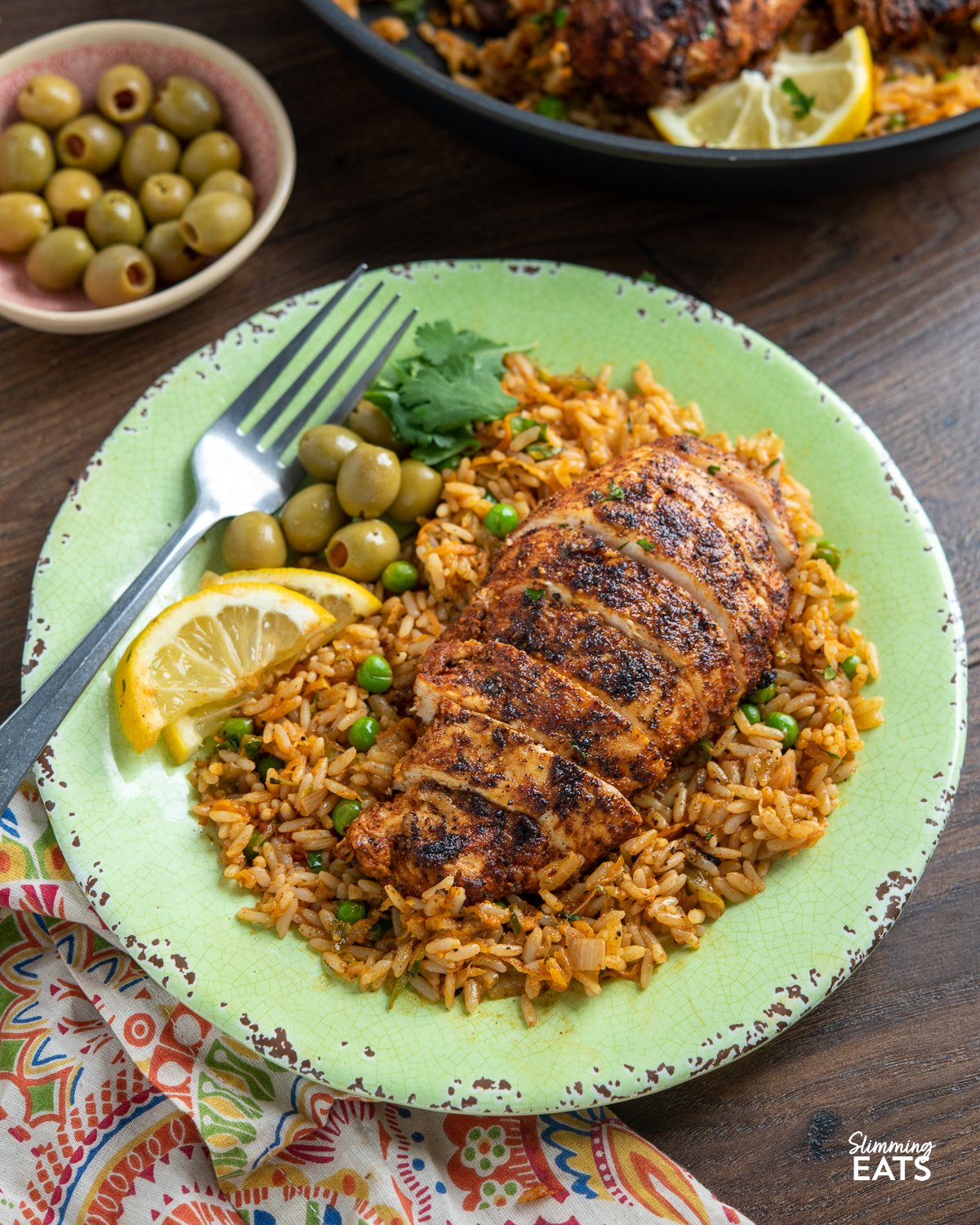 Spanish Chicken and Rice on a green plate with green olives, coriander and lemon slices