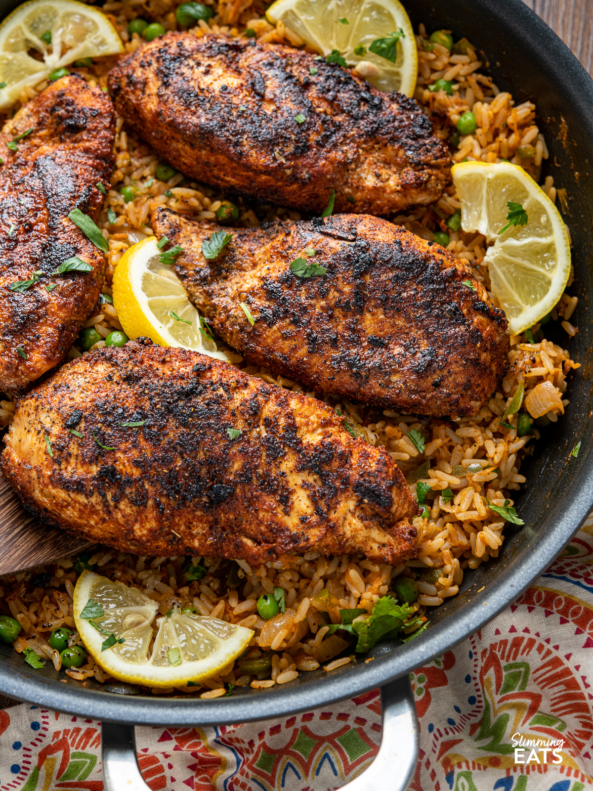 close up of Spanish Chicken and Rice in a black frying pan with wooden spatula with lemon slices