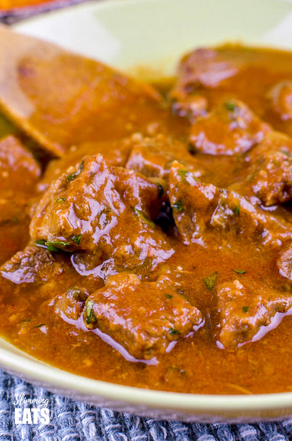 close up of slow cooked sweet onion braised beef in green bowl with wooden spoon