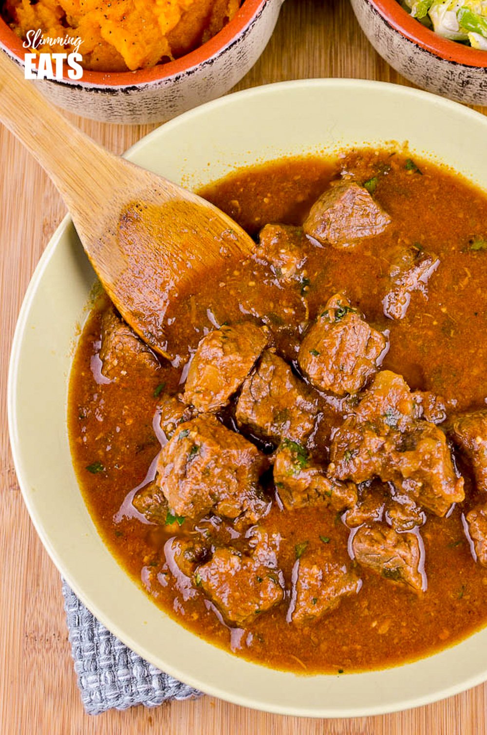 over the top view of slow cooked sweet onion braised beef in green bowl with wooden spoon