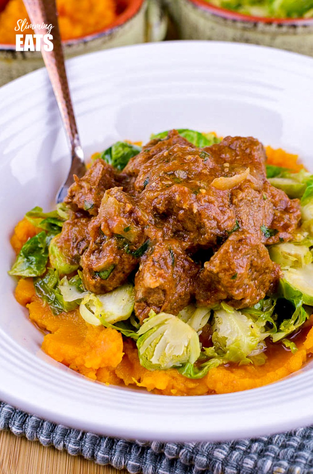 slow cooked sweet onion braised beef over sautéed Brussels and sweet potato mash in white bowl
