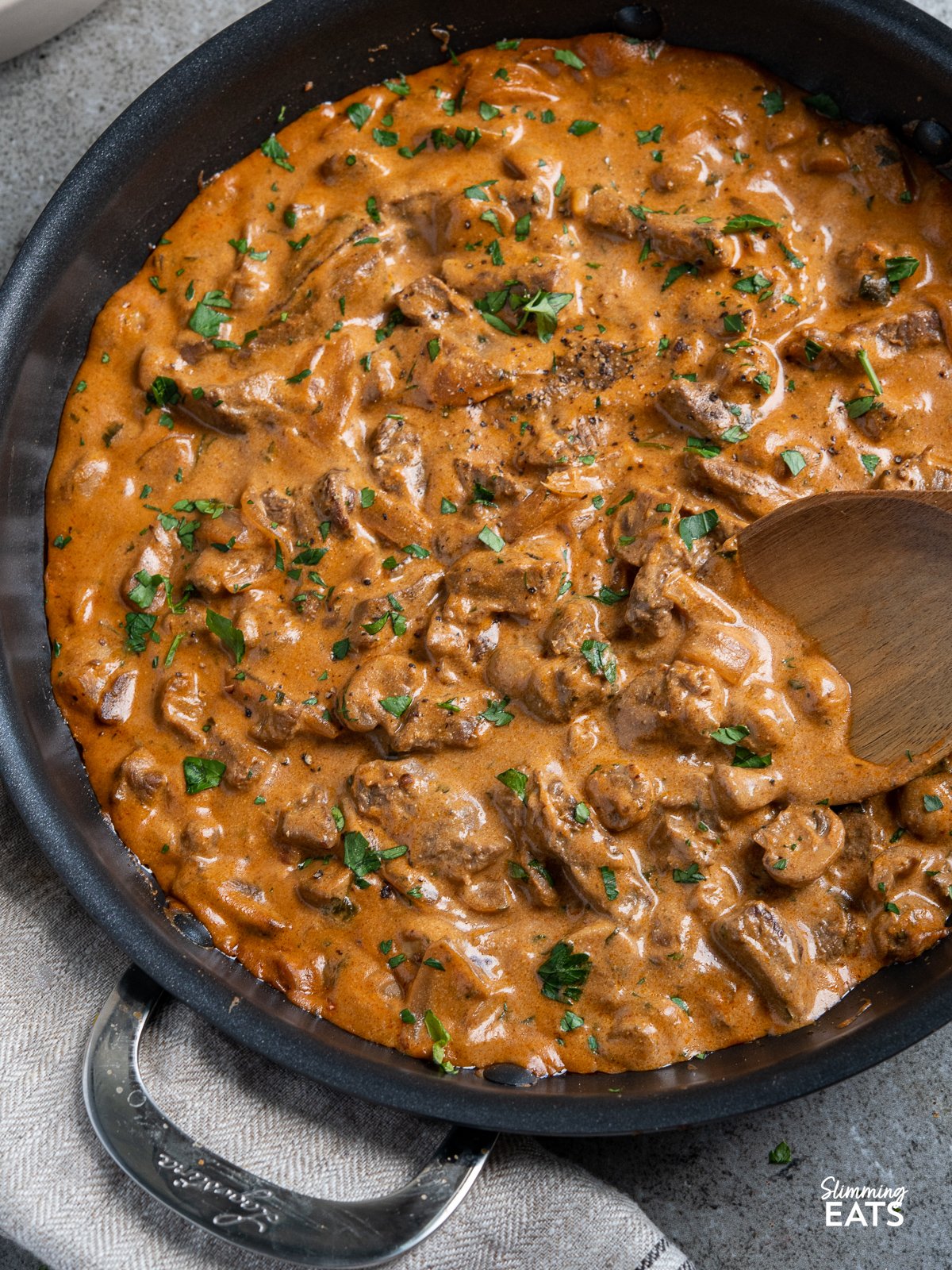 Easy homemade Lighter Beef Stroganoff - a firm family favourite, perfect with rice or noodles. close up of Beef Stroganoff in black frying pan with wooden spoon