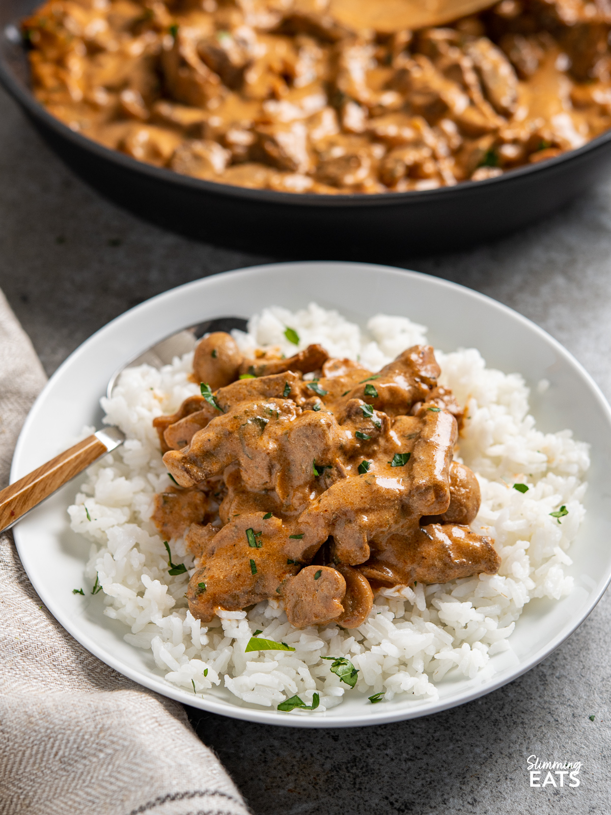 Beef Stroganoff in white bowl with rice, frying pan in background
