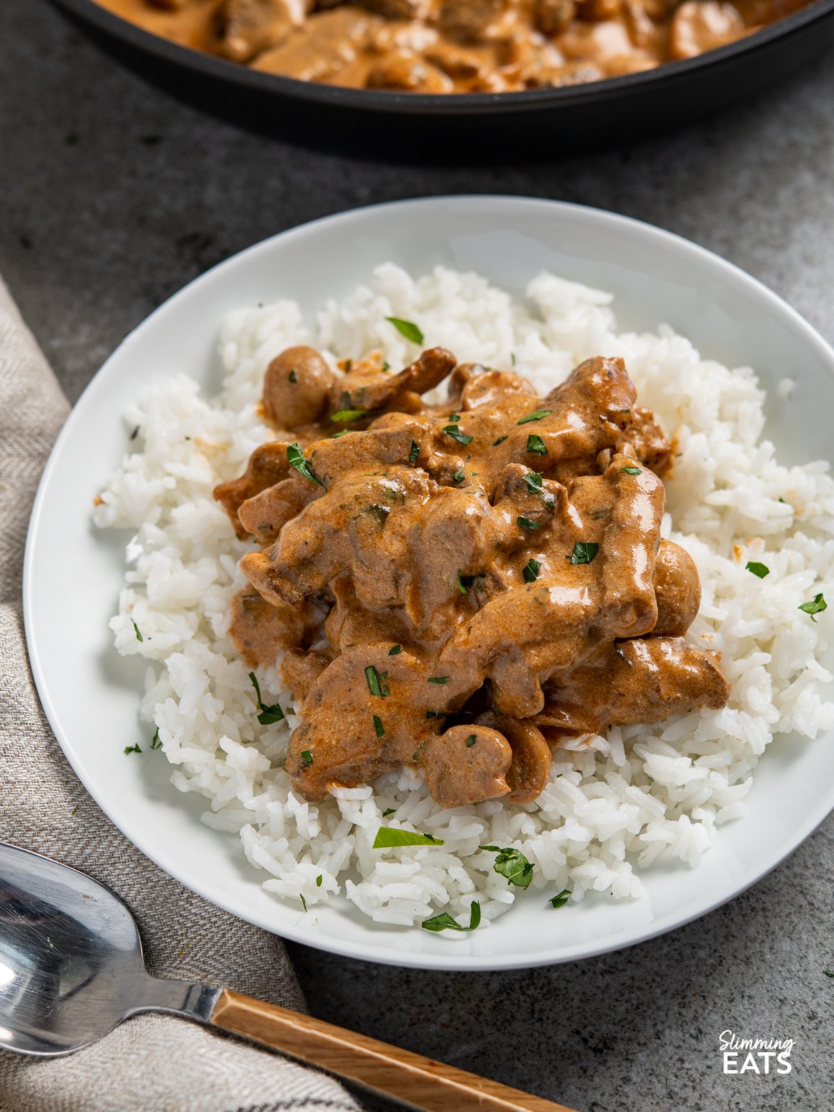 close up of Beef Stroganoff in white bowl with rice, frying pan in background