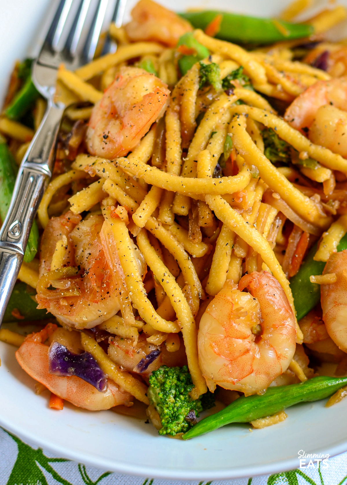 Garlic Ginger Shrimp Noodles - a quick and easy noodle dish packed with juicy shrimp, garlic, fresh ginger and a delicious savoury sauce, all ready in under 20 minutes. It is the perfect busy weeknight dinner. close up of Ginger Garlic Shrimp Noodles in white bowl with fork