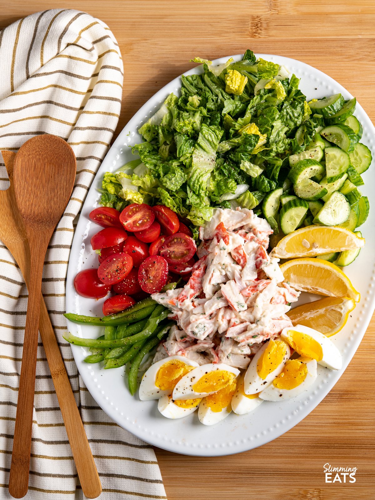 Lemon Garlic Seafood Salad on a white oval plate with salad spoons to the left