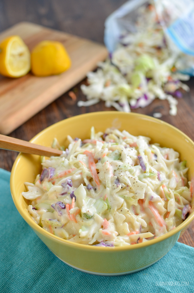 homemade coleslaw in a yellow bowl with lemon slices and shredded veg in background