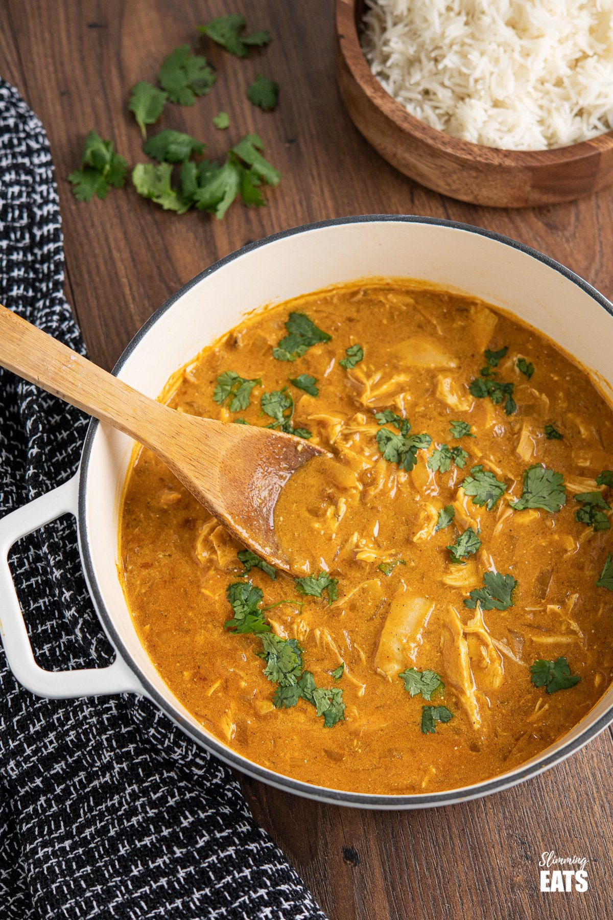 Mild chicken curry in white cast iron pan with wooden spoon and rice in background