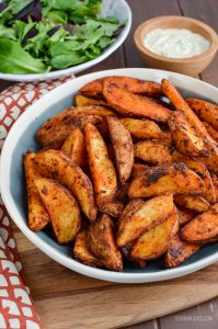 spicy potato wedges in a bowl with garlic mayo and baby greens in the background