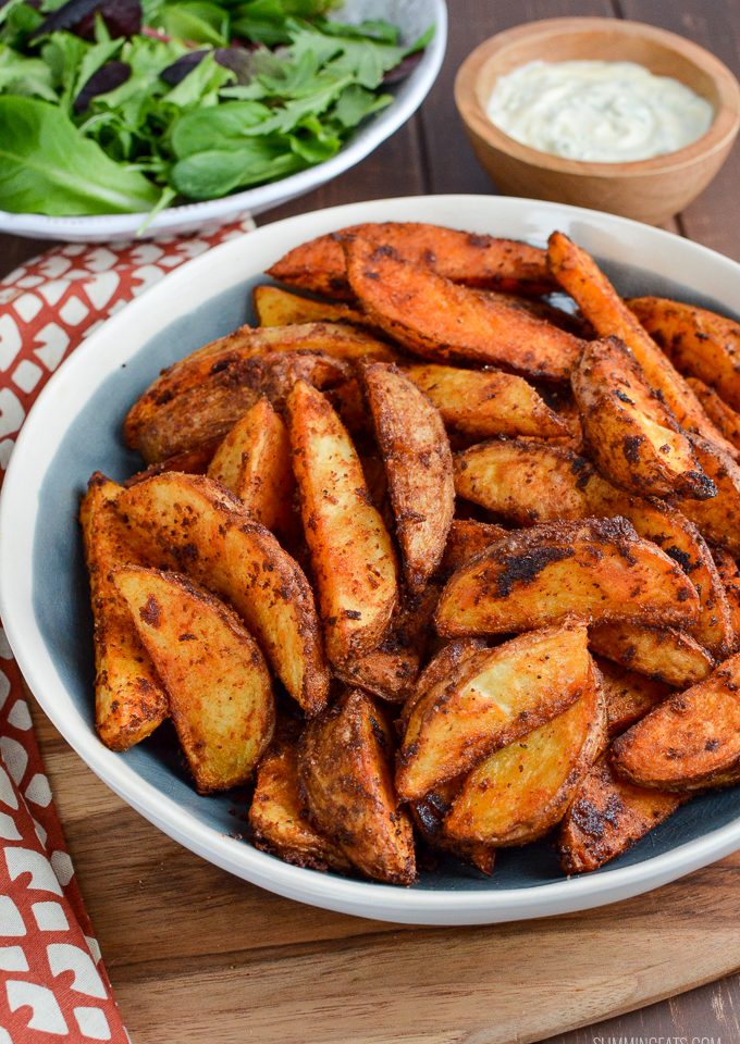 spicy potato wedges in a bowl with garlic mayo and baby greens in the background