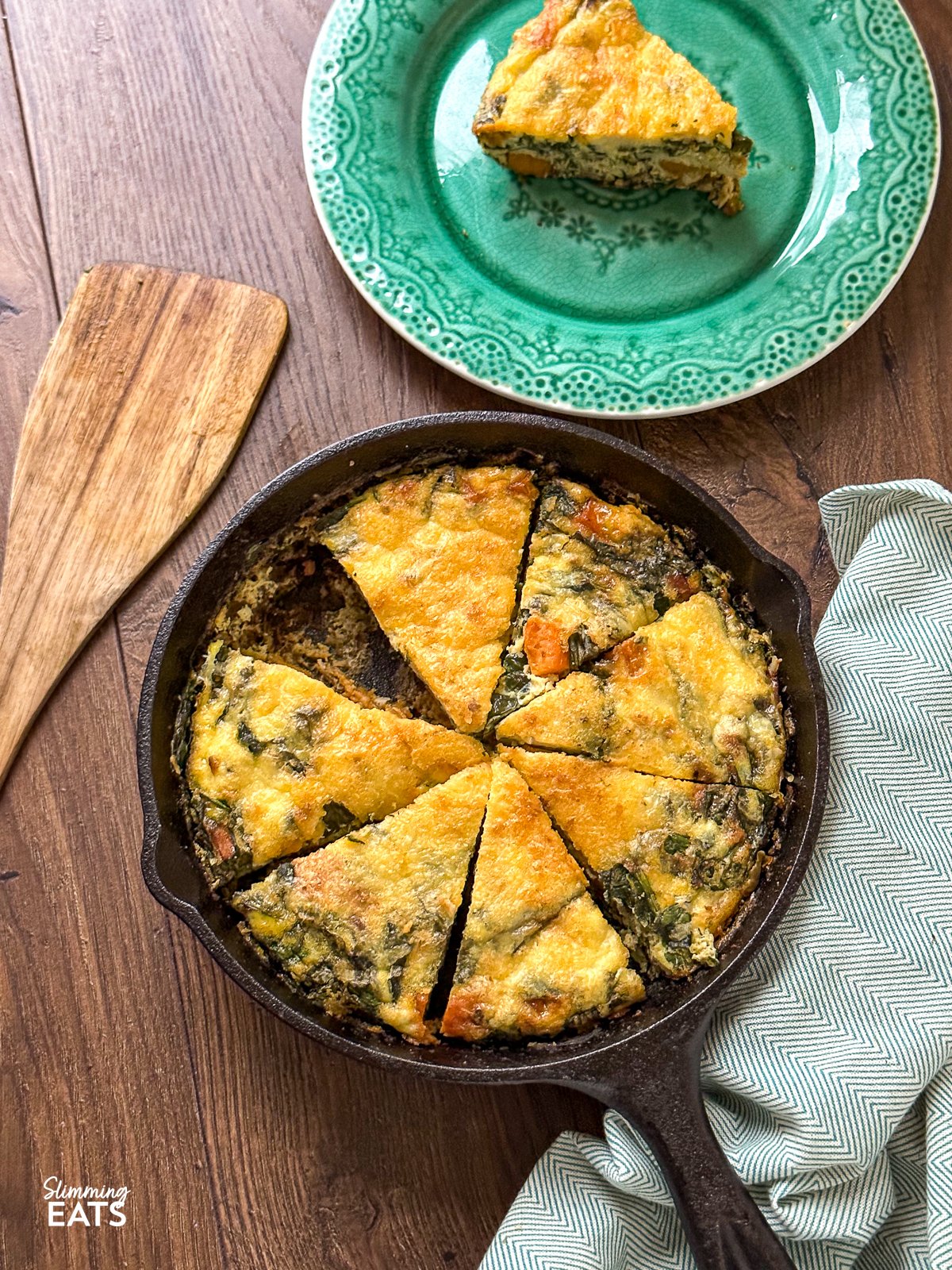 Sweet Potato and Spinach Frittata in cast iron pan sliced into 8 pieces and one slice on a teal plate