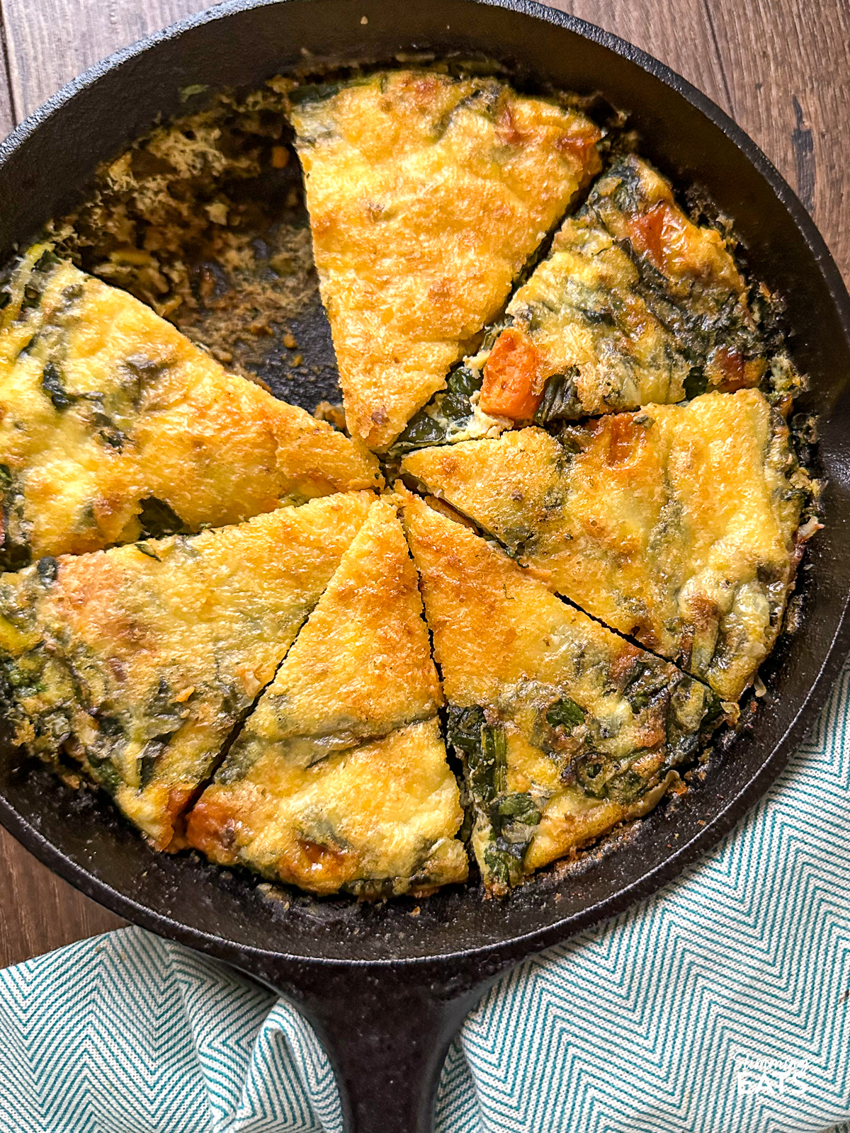 Sweet Potato and Spinach Frittata in cast iron pan sliced into 8 pieces with 1 slice removed