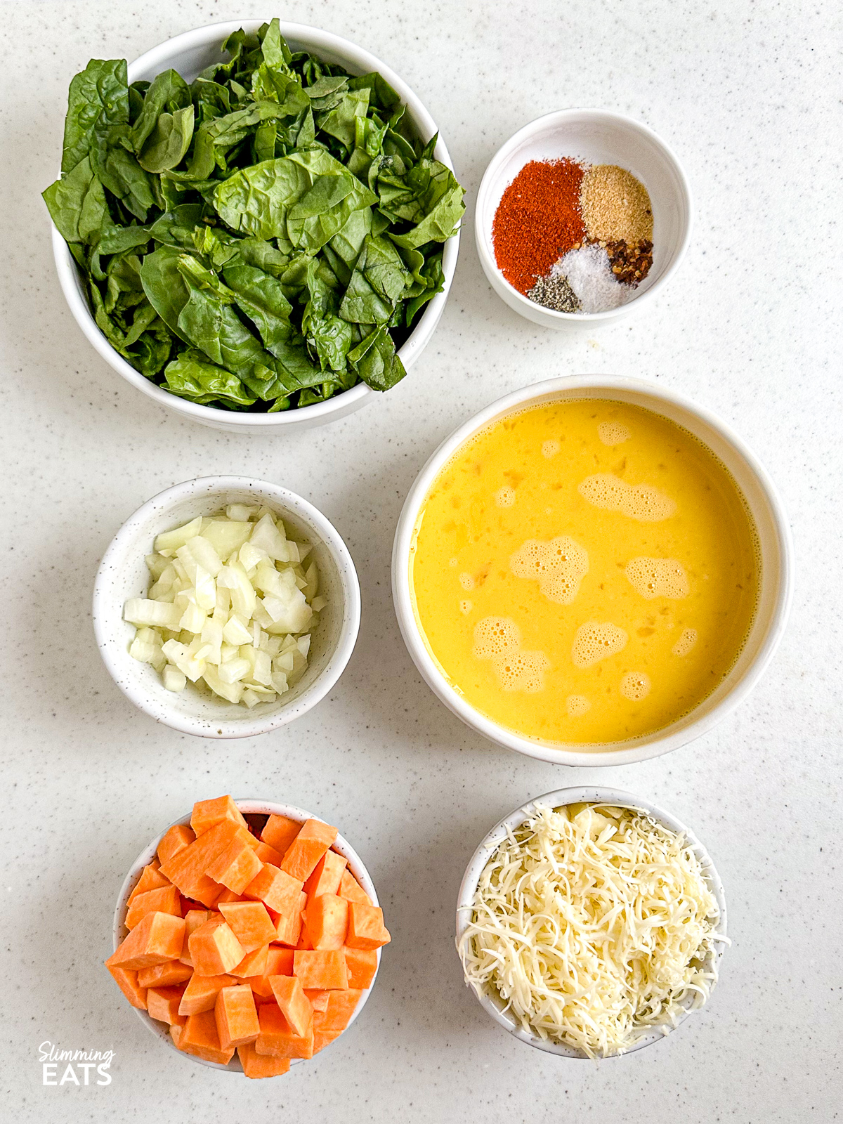ingredients in bowls to make Sweet Potato and Spinach Frittata - spinach, seasoning, onion, beaten eggs, cubed sweet potato and greated cheddar