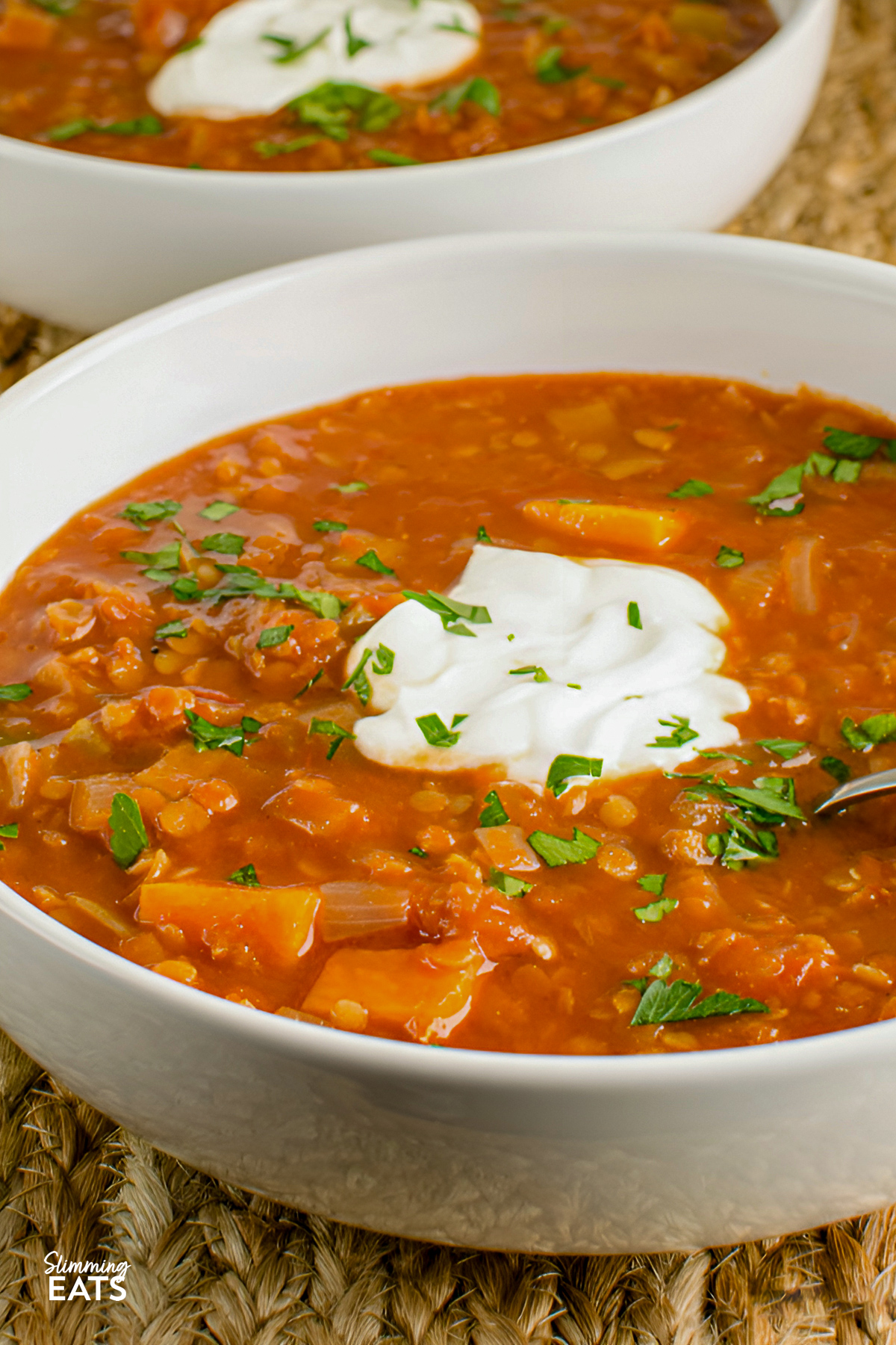Spicy tomato lentil soup served in cream-colored bowls, topped with a dollop of yogurt and sprinkled with fresh herbs.