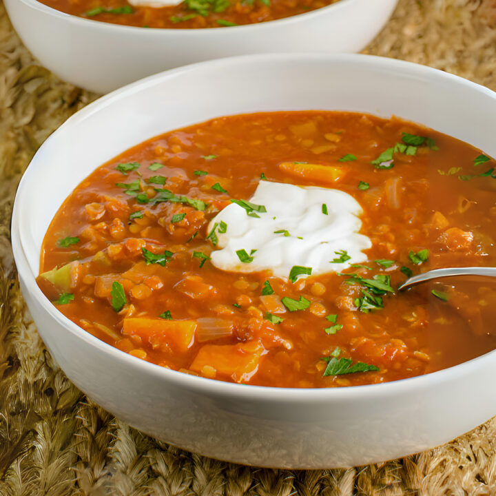 Spicy tomato lentil soup served in cream-colored bowls, topped with a dollop of yogurt and sprinkled with fresh herbs.