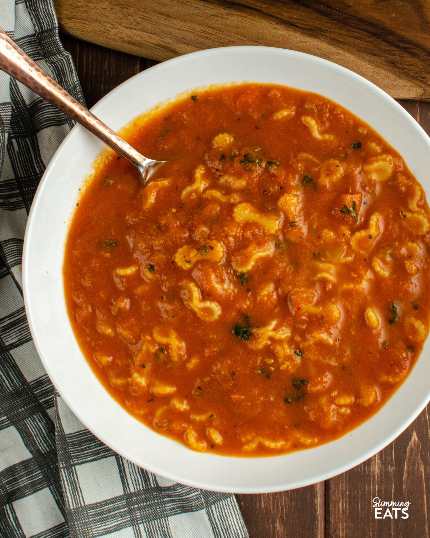 Tomato and pasta soup served in a white bowl accompanied by a spoon with a golden handle