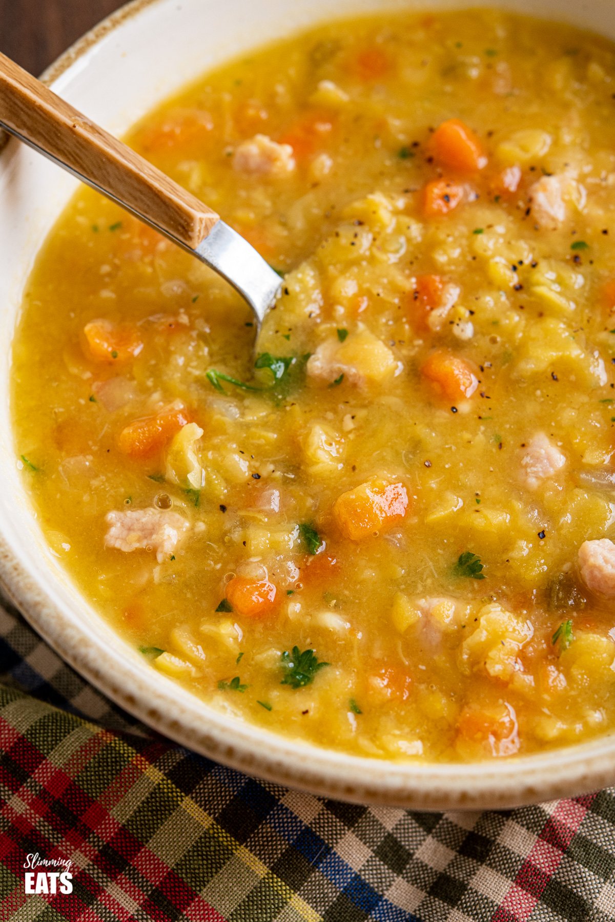 close up of split pea and bacon soup in bowl with wooden handles spoon