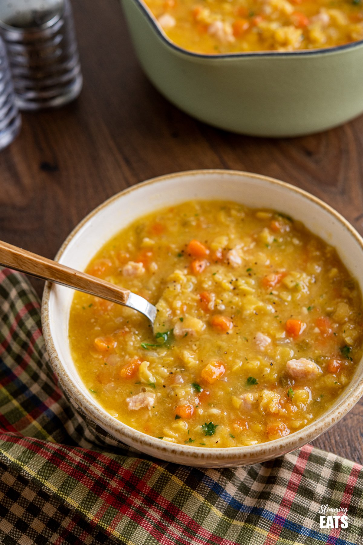 Split Pea and Bacon Soup in cream coloured bowl with wooden handle spoon 