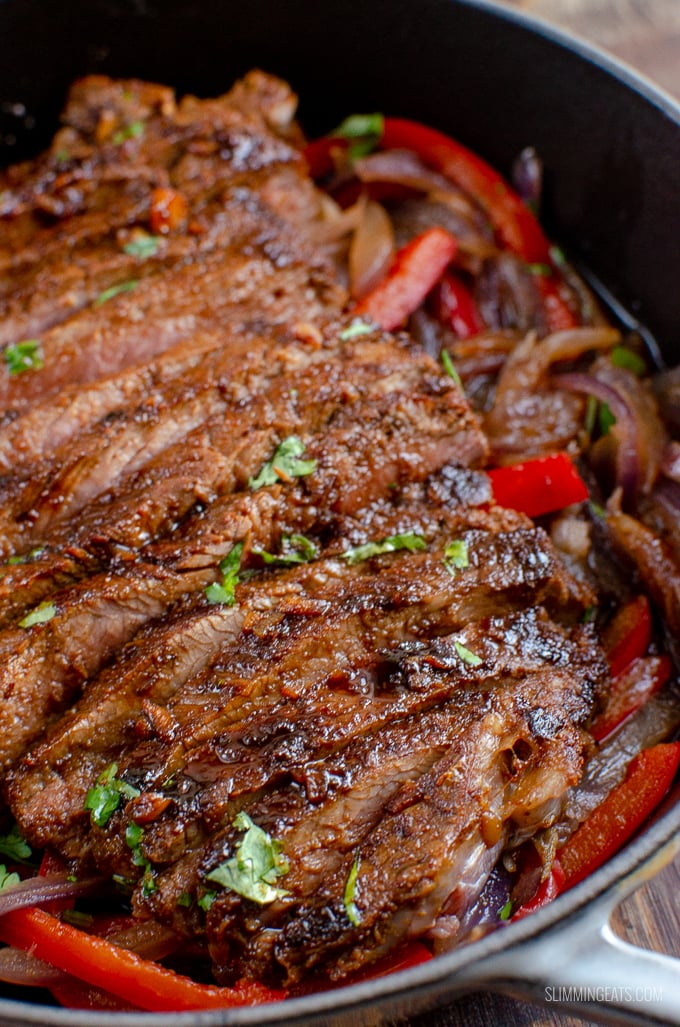 close up of Marinated Mouth-Watering Steak in cast iron skillet with peppers and onion