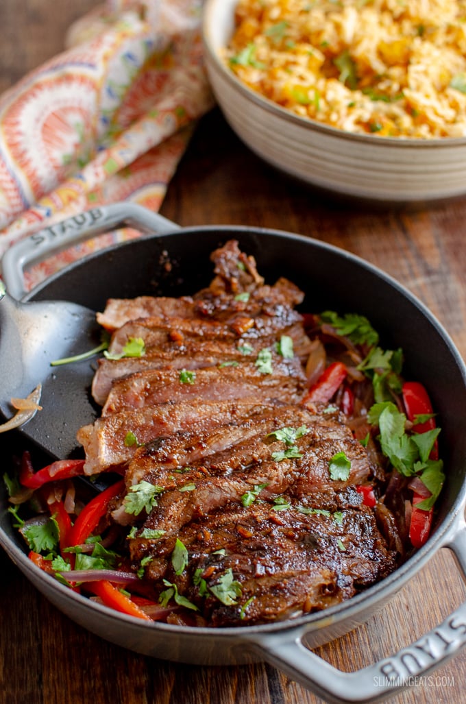 sliced marinated mouth-watering steak in a cast iron skillet with vegetables with rice in a bowl