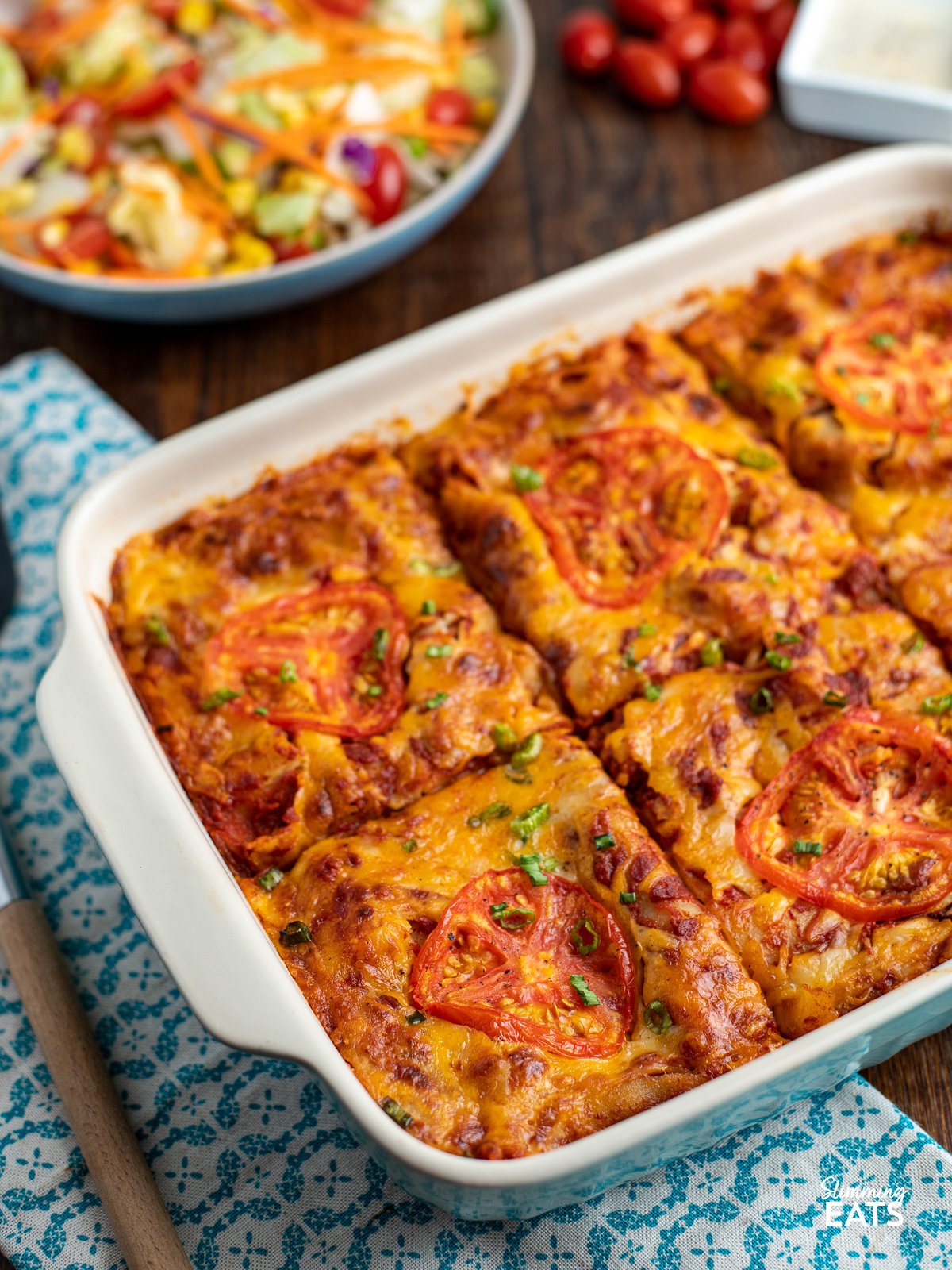 Spicy Mexican Chicken Lasagne sliced into servings in a oven baking dish, with a bowl of salad in background